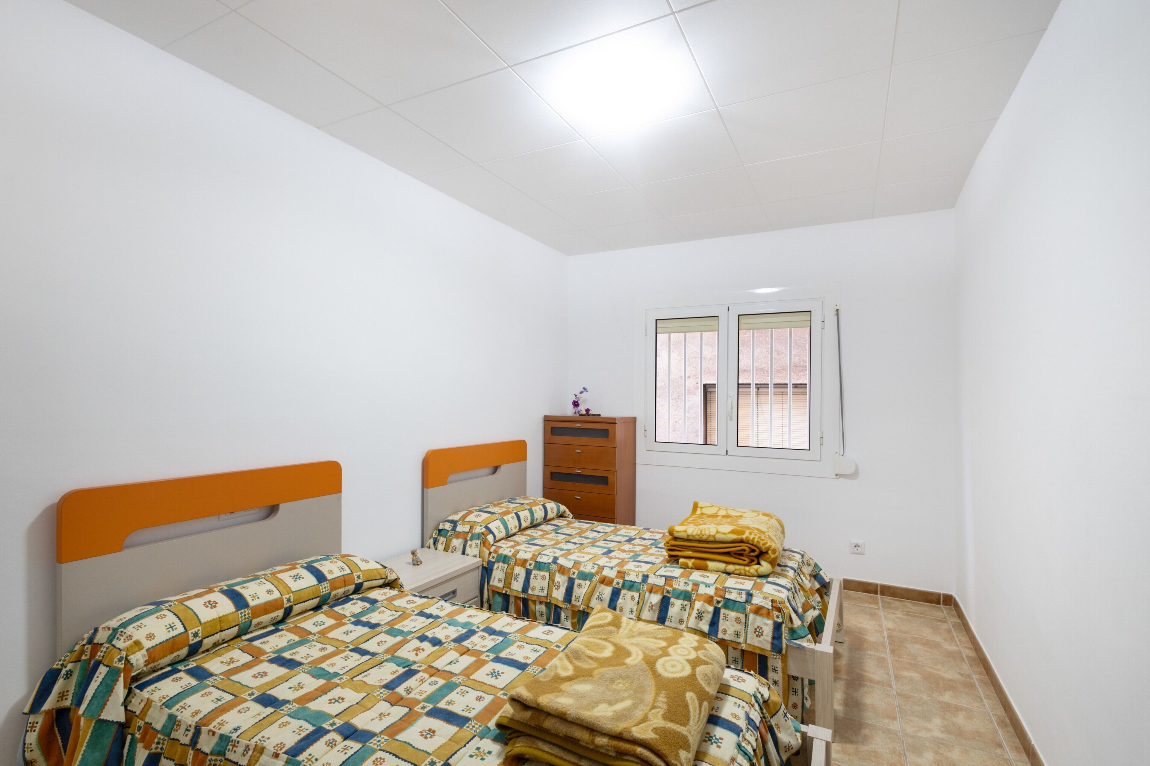 A bedroom with two beds, a dresser, a window, and a ceiling light.