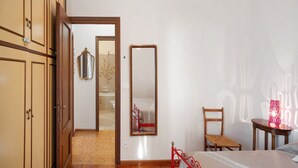A bedroom with a bed, a chair, a wooden wardrobe, a mirror, and a nightstand with a lamp. - Apartment 'Carla' with Sea View and Balcony (Sanremo)
