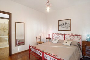Une chambre à coucher comprenant un lit, un miroir, une chaise, une table de chevet et une œuvre d’art accrochée au mur.