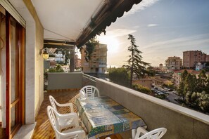 Un balcón con mesa y sillas, vista a la ciudad y un edificio al fondo.