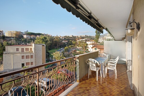 Un balcon donnant sur un quartier résidentiel, une table avec des chaises et une voiture garée à l’extérieur.