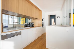 A modern kitchen with wooden cabinets, stainless steel appliances, and a dishwasher. - Le Pied-à-terre – 200m from the Beach, Close to Shops (Bénodet)