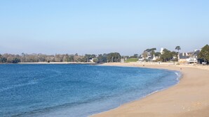 Ein Strand mit blauem Himmel, ruhigem Wasser und Gebäuden im Hintergrund.