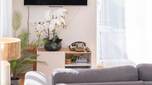 Ein Wohnzimmer mit einer Couch, einem an der Wand montierten Fernseher, einem Telefon und einer Topfpflanze.