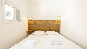 Une chambre d’hôtel avec une tête de lit en bois, deux lampes de chevet, une fenêtre ornée de vitraux et des serviettes blanches soigneusement pliées sur le lit.