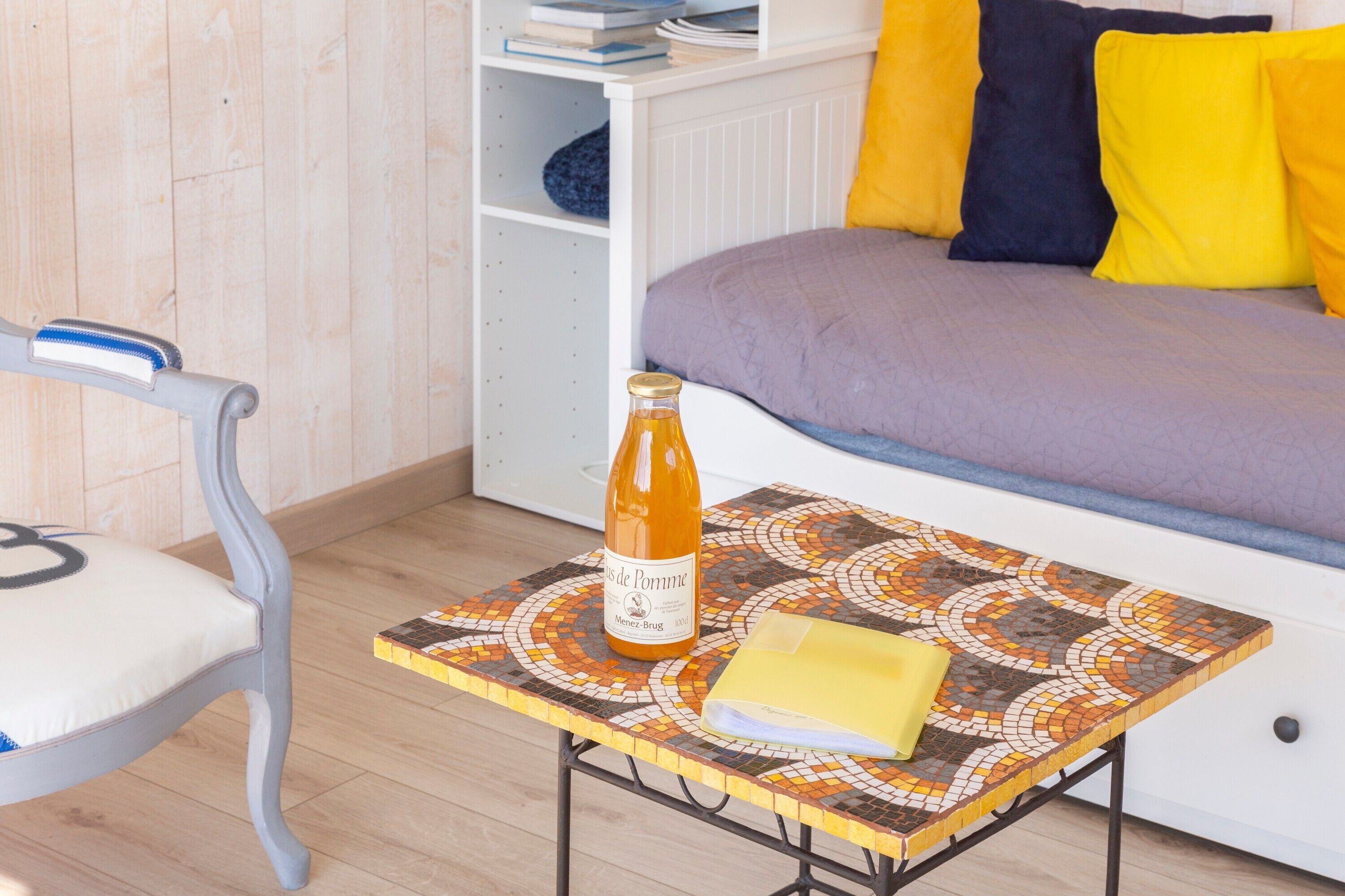 Une pièce comprenant un lit, une chaise, une table avec une bouteille et une bibliothèque.