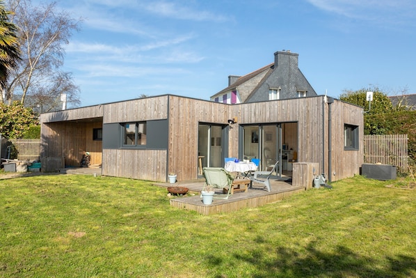 A modern house with a deck, a patio, and a fenced backyard.