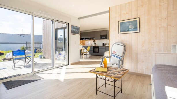 Un salon moderne doté d’une grande porte-fenêtre coulissante donnant sur un espace extérieur, d’une petite table avec une bouteille et d’un lit.