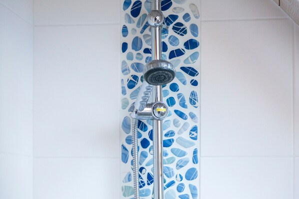 Ducha con grifo cromado y mando, frente a pared con mosaicos azules.
