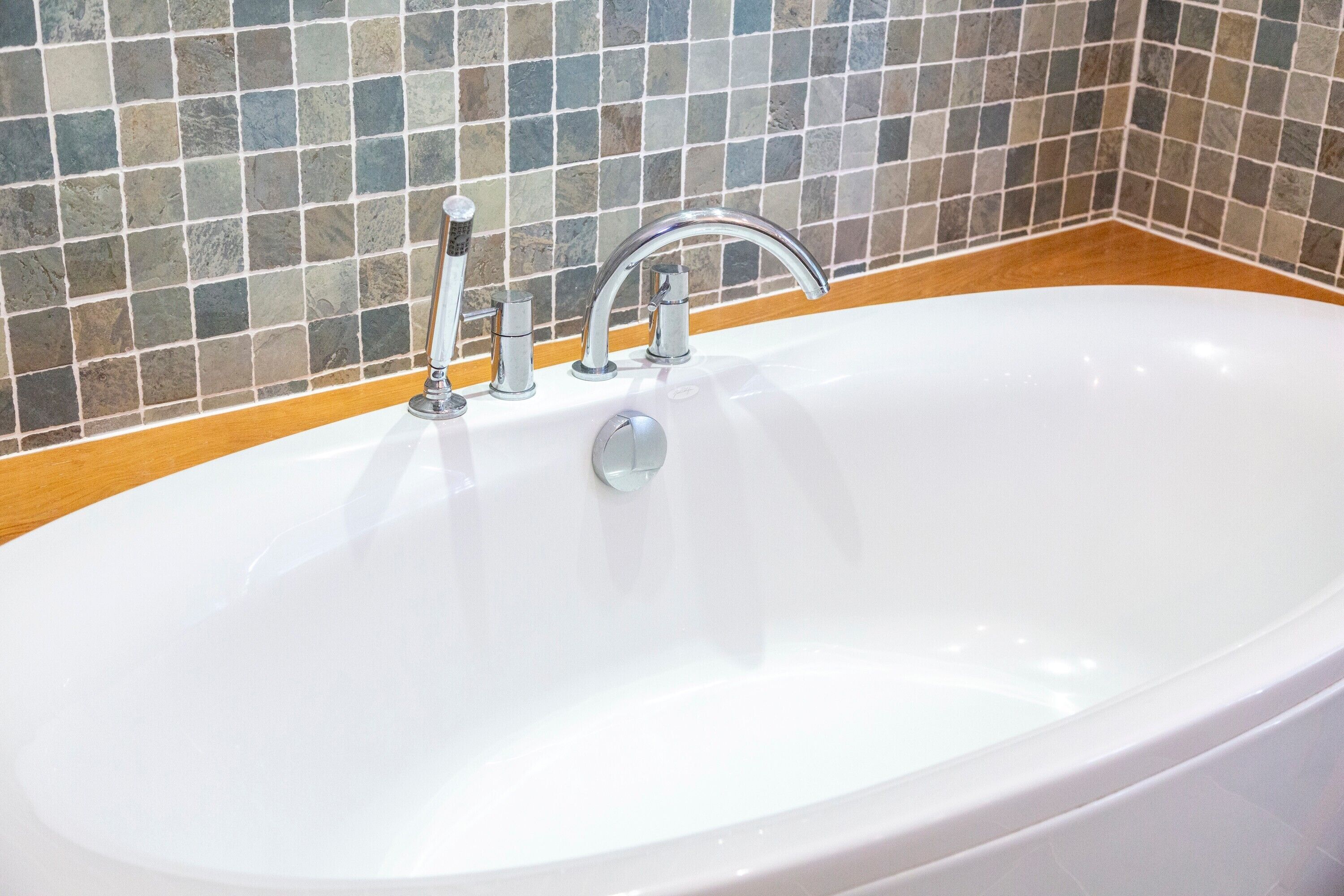 Une salle de bain moderne avec une baignoire sur pieds, un seul robinet et un mur recouvert de carreaux.