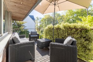 Un espace extérieur aménagé, abrité et doté de mobilier en osier et d’un grand parasol.