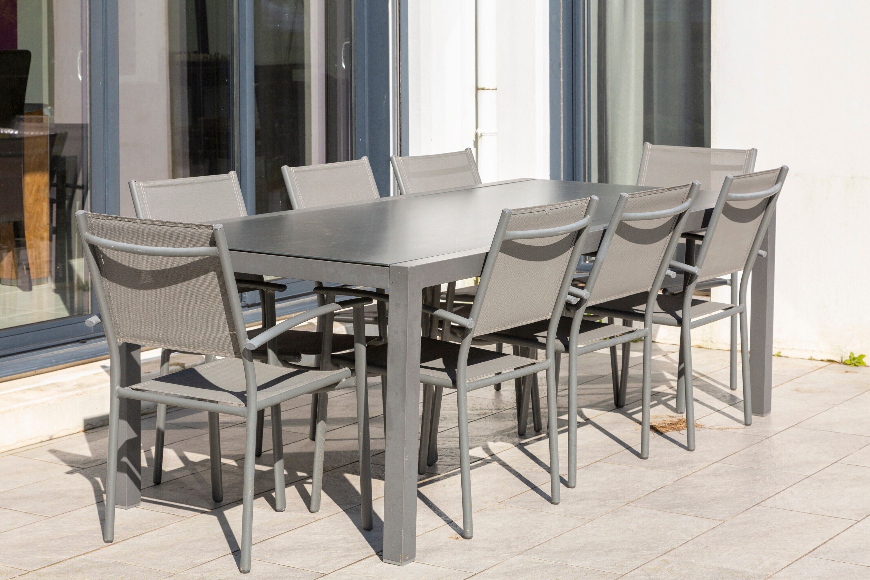 Un espacio exterior para comer con una mesa, sillas, un vidrio y suelo de baldosas.