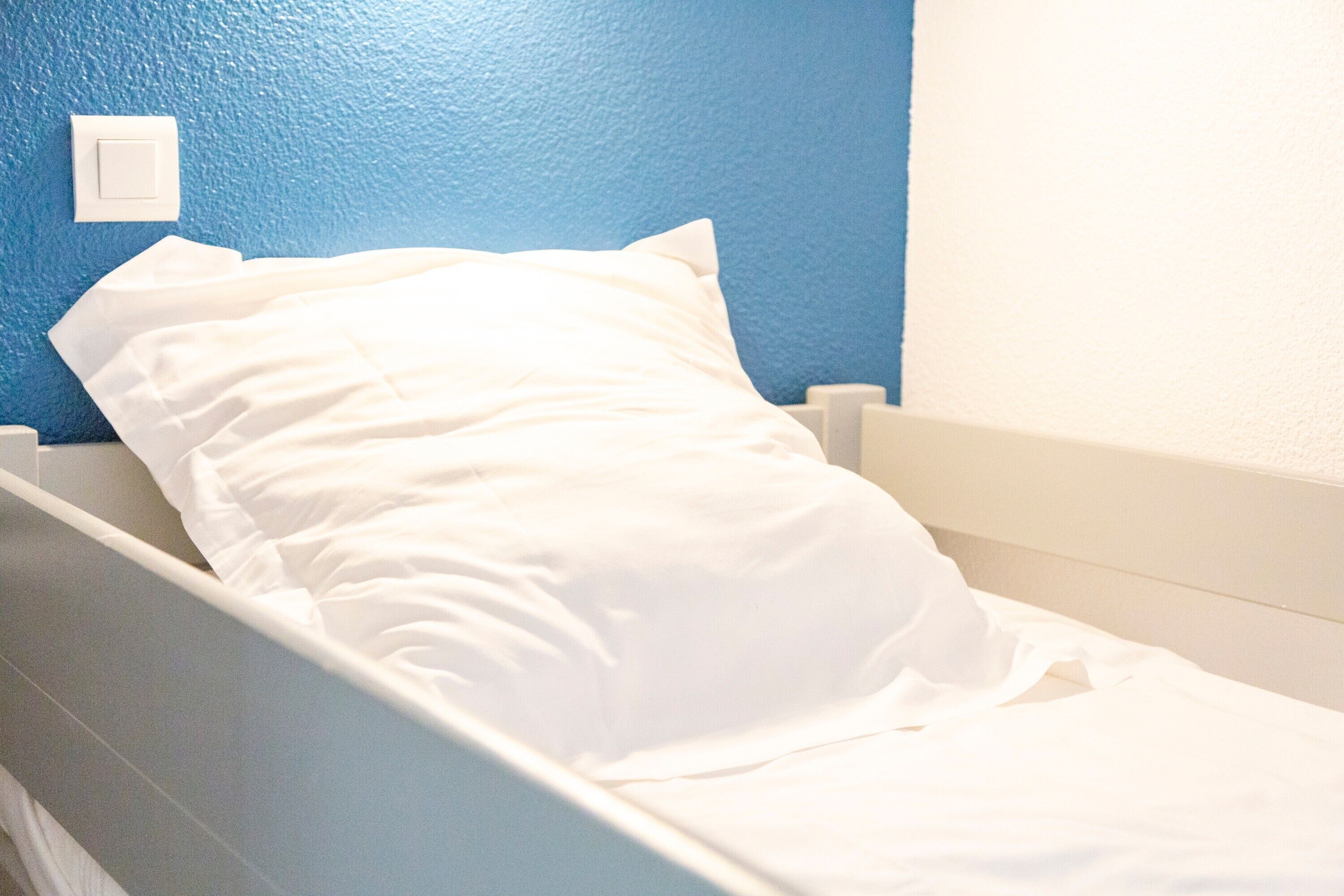 Un lit simple avec une literie blanche, dans une pièce aux murs bleus.