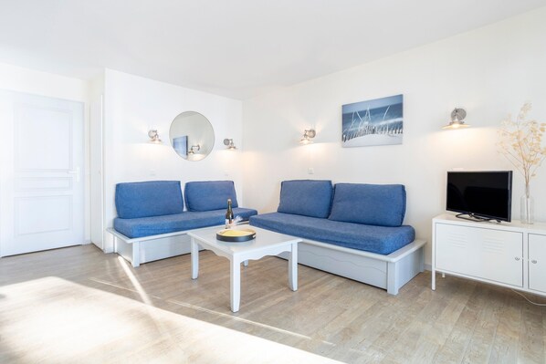 A modern living room with two blue sofas, a white coffee table, a television, and a cabinet.