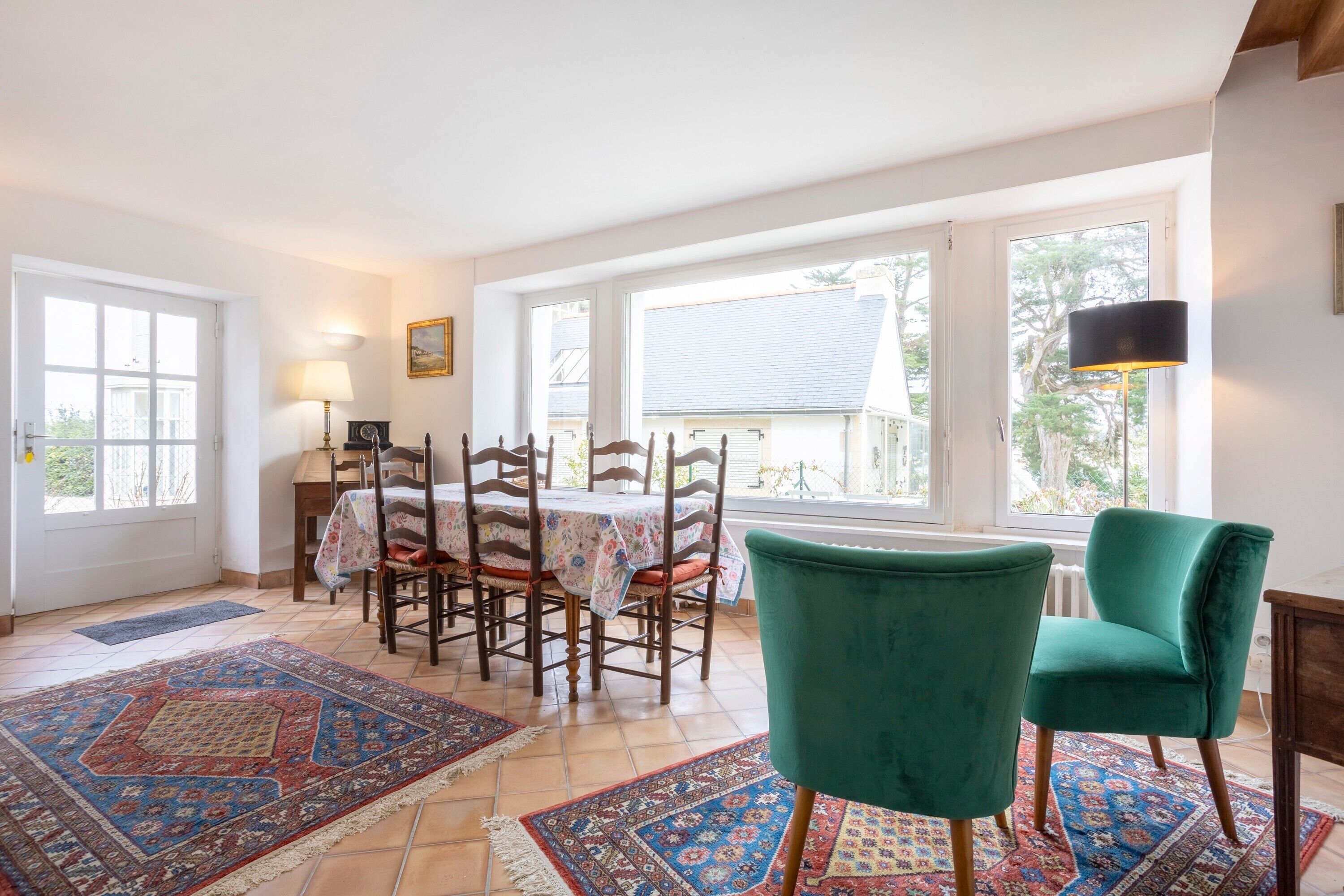 Un comedor con una mesa preparada para cuatro personas, un sillón verde y una alfombra estampada.