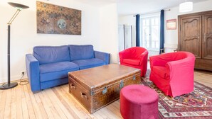 A living room with a blue sofa, a red armchair, a wooden chest, and a red ottoman. - L'Estuaire – River View, 20 Meters from Shops (Combrit)