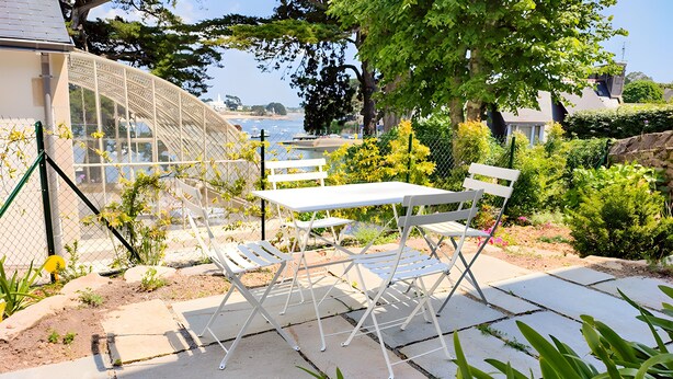 A patio with a white table and chairs, a glass greenhouse, and a view of the sea. - L'Estuaire – River View, 20 Meters from Shops (Combrit)