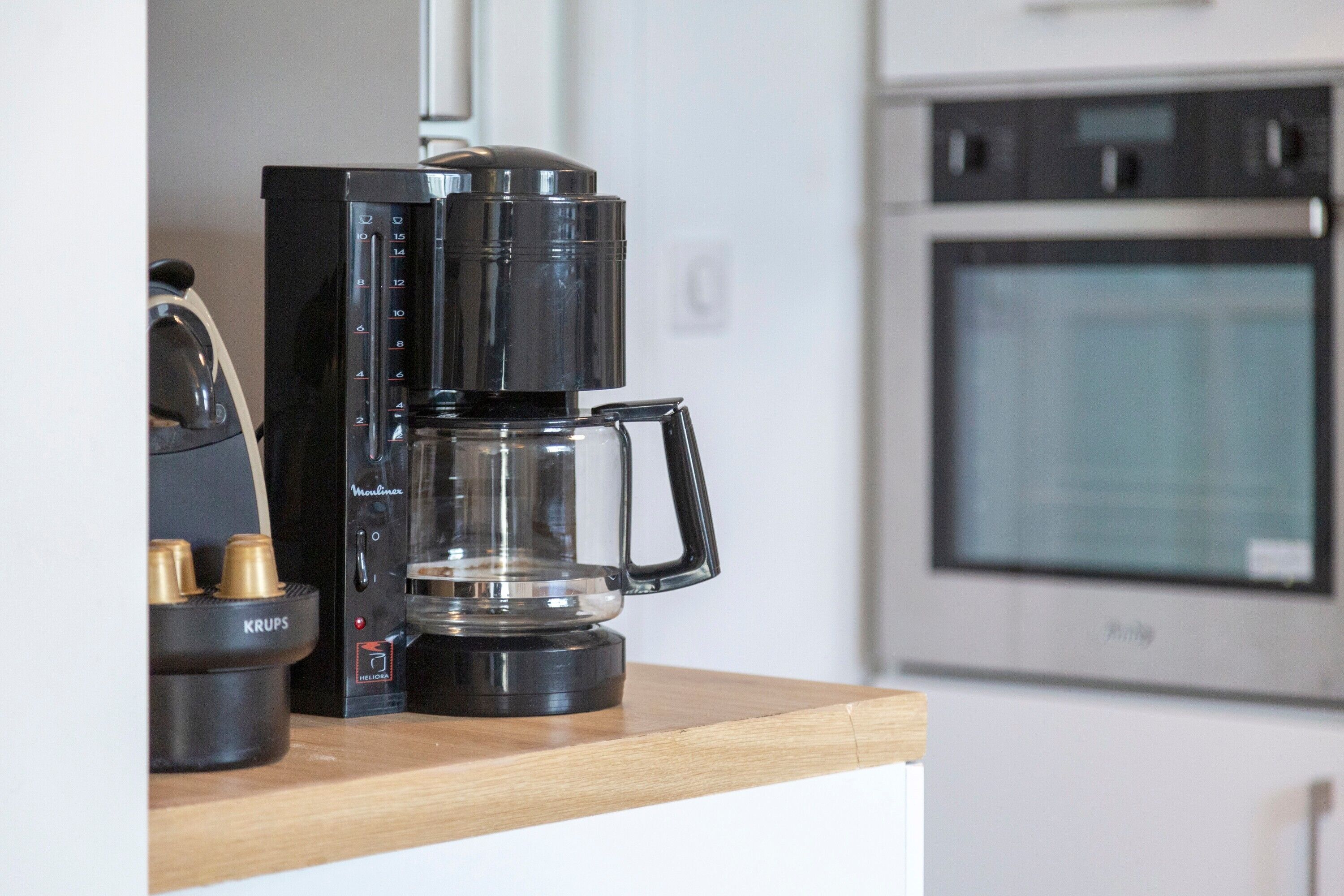 A coffee maker on a wooden countertop in a kitchen with an oven in the background.