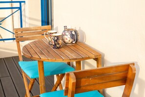 A wooden table with a floral teapot and cups, a wooden chair, and a blue cushion.