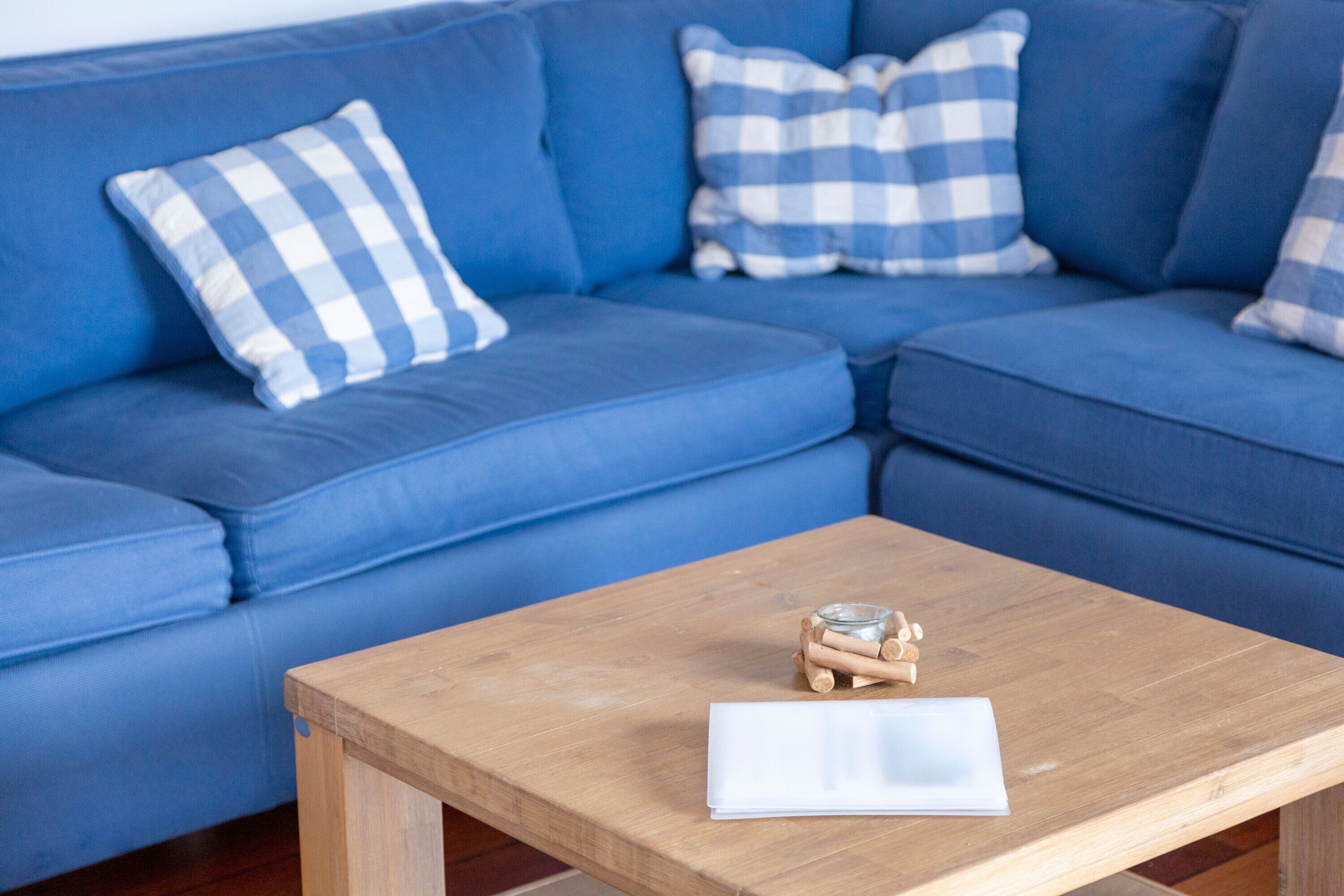 Un canapé bleu avec des coussins à carreaux, une table en bois sur laquelle se trouvent un objet en verre et un objet blanc.