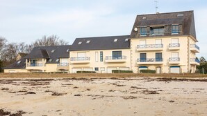 Een meerhoog gebouw met balkons, een plat dak en een zandkleurige voorgrond.