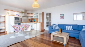Een moderne woonkamer met een blauwe bank, een salontafel en een keuken met een magnetron en kastjes.