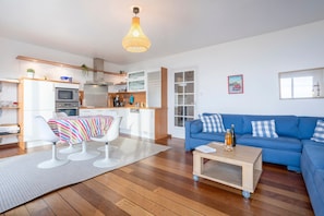 A modern living room with a blue sofa, a coffee table, and a kitchen area with a microwave and cabinets.