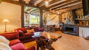 Een rustiek interieur met een stenen openhaard, houten balken, een rode bank en een houten bijzettafeltje.