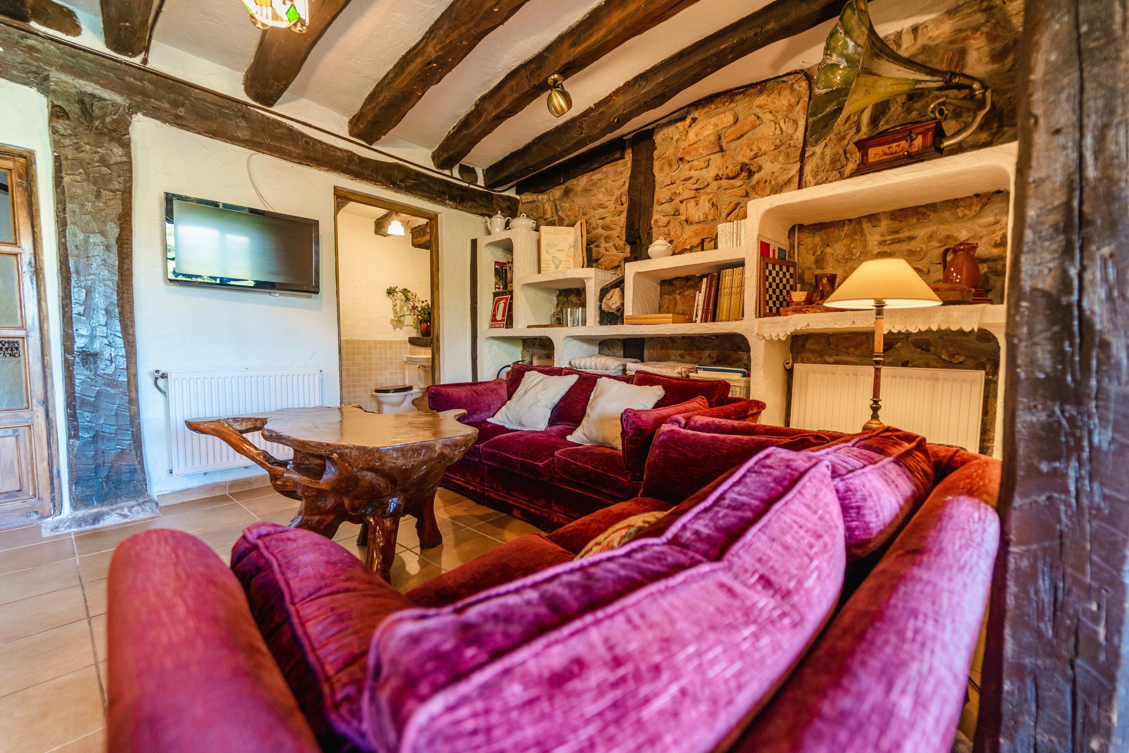 Ein gemütliches Wohnzimmer mit Steinwand, Holzbalken, einem roten Sofa und einem an der Wand befestigten Fernseher.