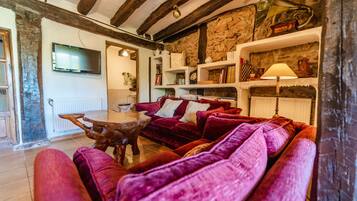 Ein gemütliches Wohnzimmer mit Steinwand, Holzbalken, einem roten Sofa und einem an der Wand befestigten Fernseher.