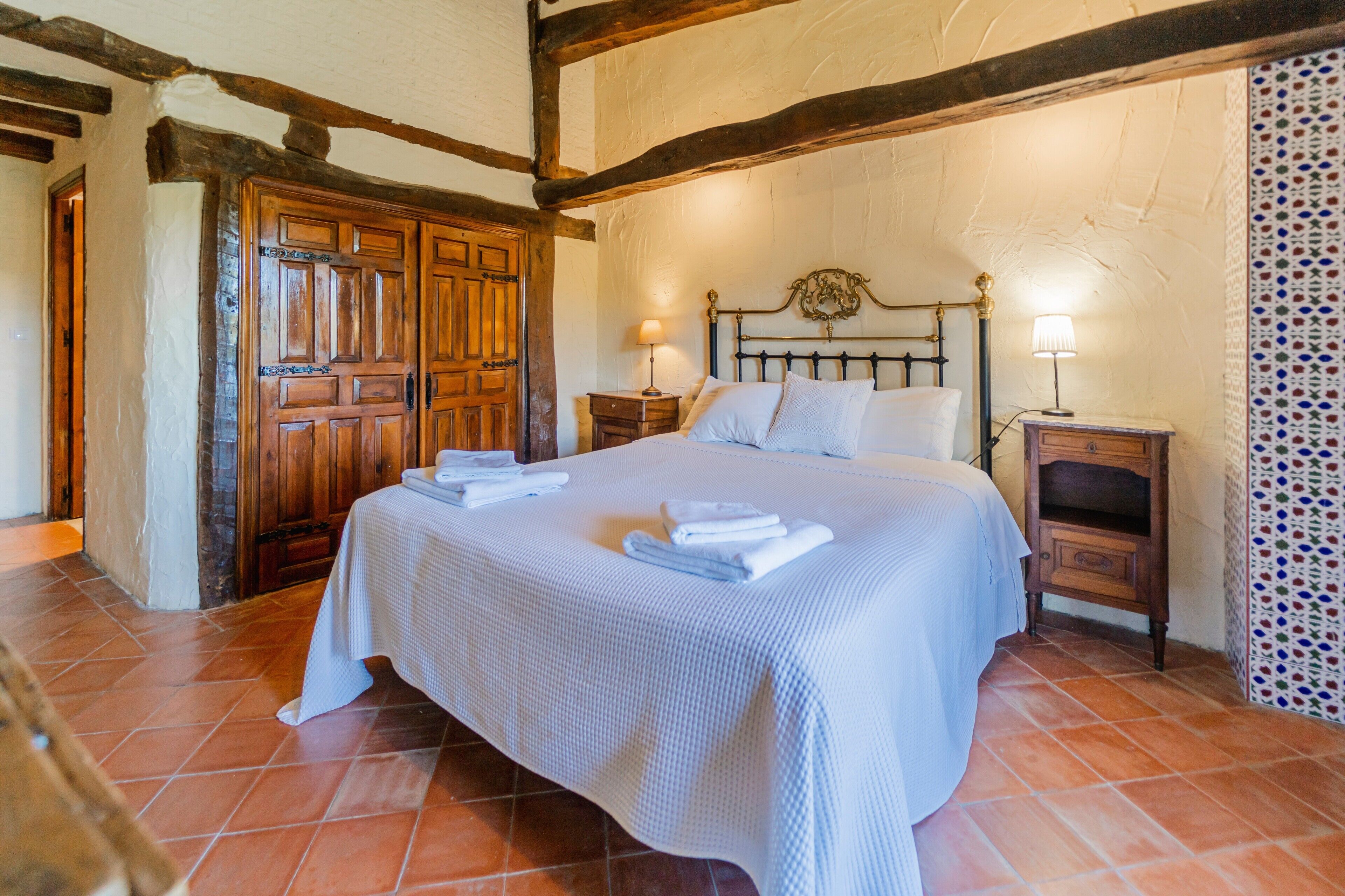 Un dormitorio con una cama grande, cabecera de madera, dos mesitas de noche con lámparas y un papel tapiz decorado.