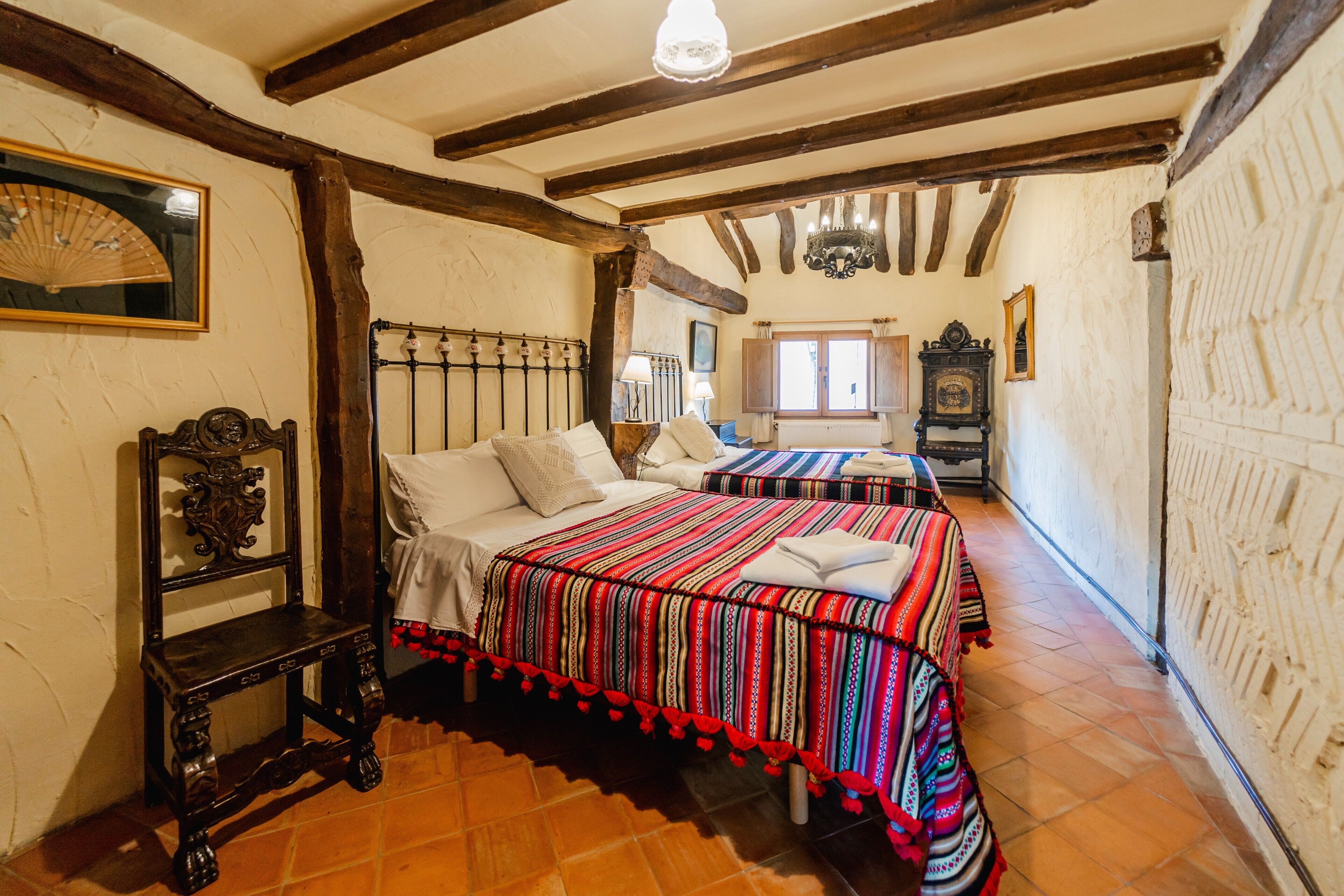 Una habitación tradicional con vigas de madera a la vista, una cama con colcha a rayas, una silla de madera y una ventana con vistas.