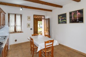Zona pranzo con tavolo e sedie, cucina con lavello e due opere d'arte incorniciate al muro.