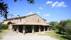 Un edificio in pietra con tetto a tegole, un portico coperto e un vialetto sterrato.