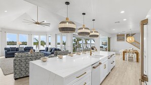 A spacious living area with a large island, a dining area, and a kitchen with white cabinetry and a marble countertop.