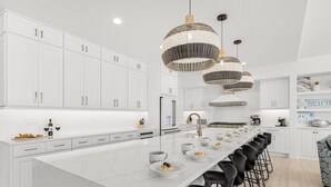A modern kitchen with white cabinetry, a large island with bar stools, and decorative woven pendant lights.