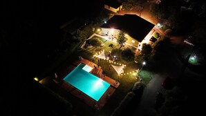 Vue aérienne d’une propriété résidentielle de nuit, avec une piscine, un éclairage extérieur et une pelouse bien entretenue.