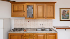 Une cuisine avec des meubles en bois, un évier en acier inoxydable, une cuisinière à gaz et un dosseret carrelé.