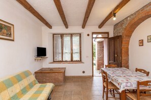Una habitación con sofá, televisión, mesa con sillas, ventana con cortinas y pared de ladrillo.