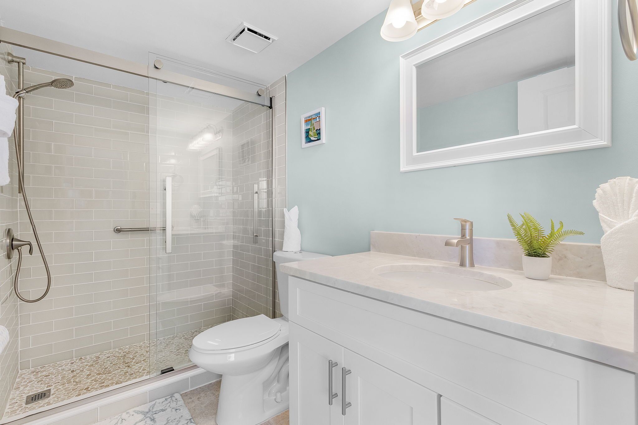 Un baño moderno con ducha de vidrio, inodoro blanco y tocador con lavamanos y espejo.