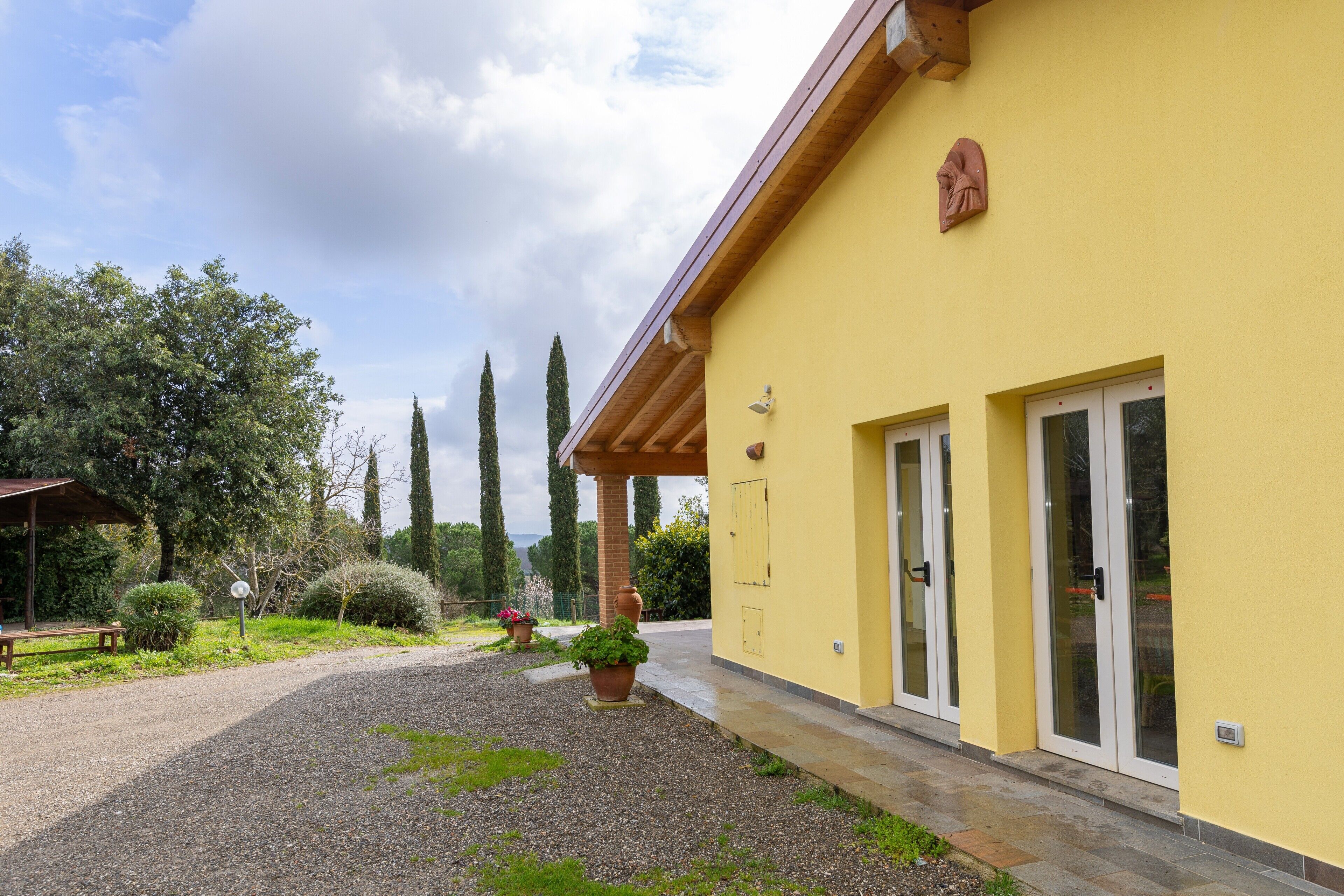 A yellow building with a covered entrance, a gravel driveway, and a bench.