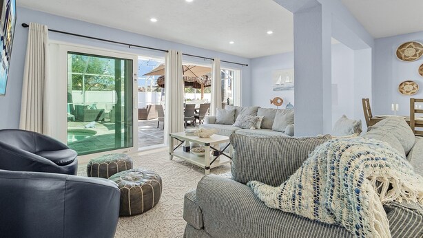 A modern living room with a sofa, ottoman, and a coffee table. There is a sliding glass door leading to an outdoor patio area.