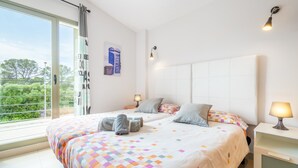 Een hotelkamer met twee bedden, een groot raam, uitzicht op groen en een wit hoofdeinde.