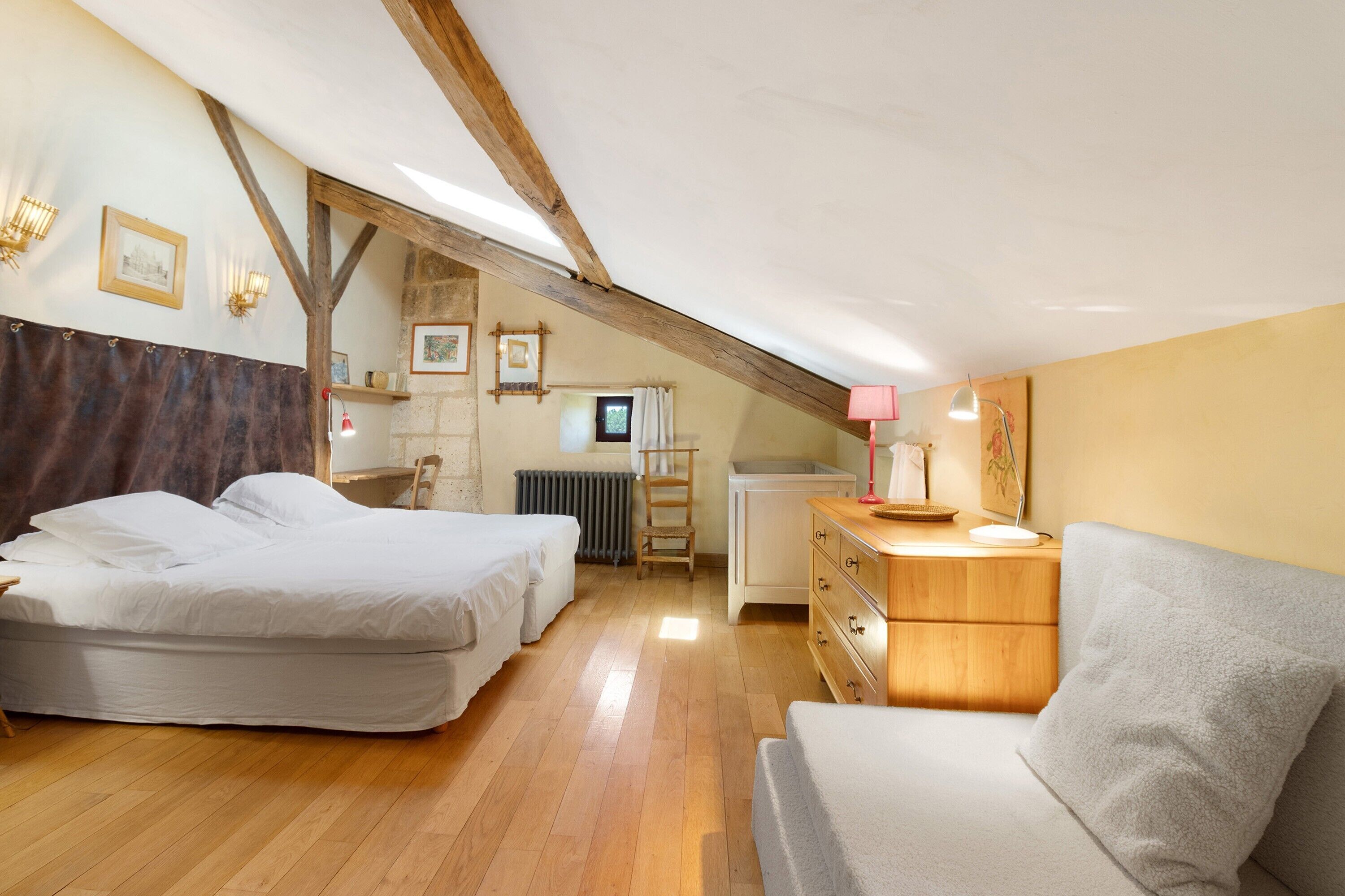 Une chambre avec deux lits, une commode en bois, une chaise et un bureau avec une lampe.