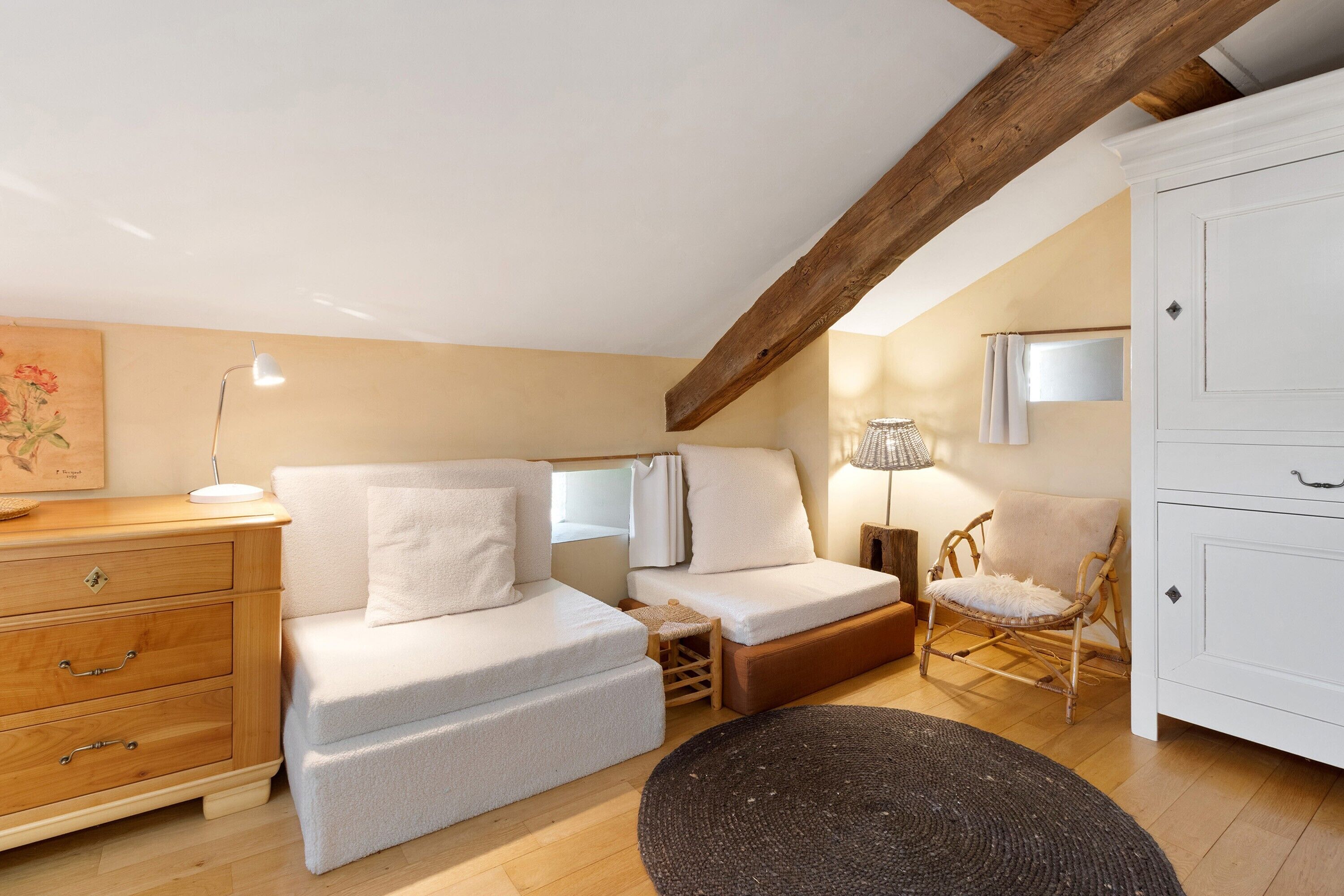Une chambre mansardée chaleureuse, avec un lit en mezzanine, un canapé, un fauteuil, une commode et une lampe.