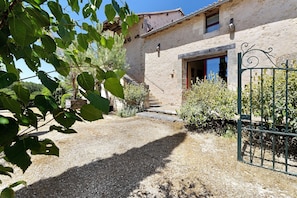 A rustic stone building with a gravel path leading to a wooden door, surrounded by greenery.