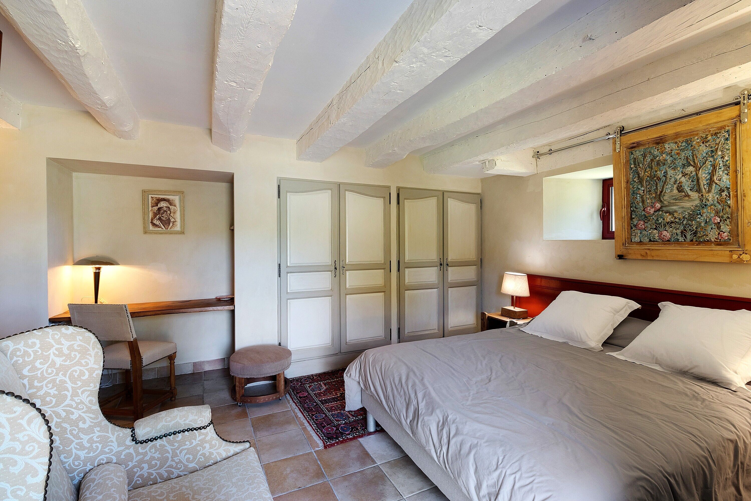Un dormitorio con una cama, una silla, un escritorio, un armario y un cuadro en la pared.