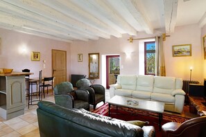 Een woonkamer met een witte bank, een groene leren bankstel en twee fauteuils met een patroon.