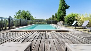 Une terrasse en bois avec une piscine, des chaises longues et une clôture.