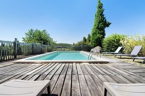 A wooden deck with a swimming pool, lounge chairs, and a fence.